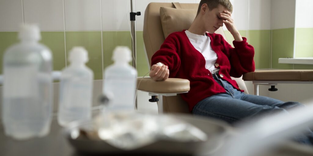 Junger Mann sitzt erschöpft im Infusionsstuhl