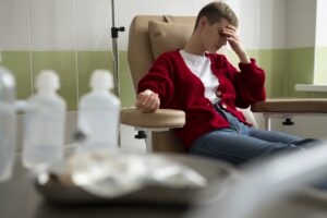 Junger Mann sitzt erschöpft im Infusionsstuhl